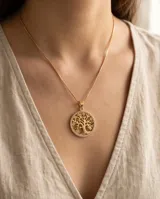 Collar de bronce dorado con cadena fina y dije circular colgante con diseño del árbol de la vida rodeado de incrustaciones de pedrería.