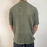 Camisa de tejido de punto calado en color beige, con cuello polo, cierre frontal de botones y mangas cortas.
