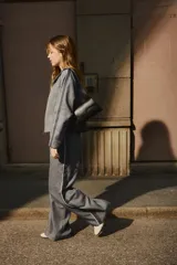 Pantalón de vestir gris oscuro con finas rayas verticales blancas (pinstripe), tiro alto y cintura elástica con cordón blanco ajustable. Presenta un corte ancho y recto, con una fina franja blanca lateral que recorre la pierna.