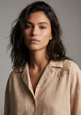 Camisa negra de manga corta con cuello tipo solapa y botones frontales. Presenta bordados sutiles en tono negro en las mangas y en la parte inferior delantera.