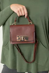 Cartera negra de cuero sintético con broche metálico dorado y asa corta. Incluye correa larga desmontable para usar como bandolera.