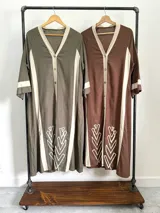 Vestido camisero marrón con rayas verticales color crema, de corte recto y largo midi. Presenta cuello en V, cierre frontal con botones y bordados en el ruedo.