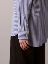 Camisa Calvin Klein de corte regular, con diseño de rayas verticales en tonos azul y blanco. Cuenta con cuello camisero, cierre frontal de botones, mangas largas y un bolsillo aplicado en el pecho con el logo bordado de la marca.