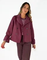 Chaqueta color tostado de corte recto y diseño cruzado con doble botonadura frontal. Presenta cuello solapa y mangas largas con puños acampanados y fruncidos.