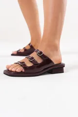 Sandalias de cuero bordó con diseño de tres tiras con hebillas metálicas regulables, punta cuadrada y taco bajo.