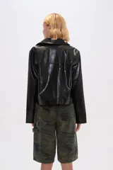Chaqueta corta de eco-cuero negra con cuello camisero, cierre frontal con botones plateados y bolsillos simulados con botones plateados.