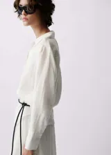 Camisa de lino color blanco, de corte recto y calce regular, con cuello camisero, cierre frontal de botones y mangas largas con puños abotonados.