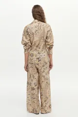 Pantalón de pierna ancha y tiro medio, confeccionado en mezcla de lino y viscosa, con cintura elástica y cordón ajustable. Presenta un estampado artesanal en tonos beige y marrón.