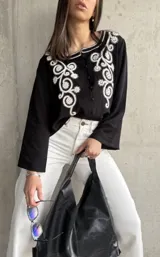 Camisa negra de manga ancha con bordado floral blanco en el frente y cierre con botones.