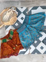 Short de seda con elástico fruncido en la cintura y volado en el ruedo. Presenta un estampado vibrante en tonos rojo/bordó y turquesa con motivos florales o arabescos.