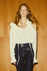 Jean de denim de algodón con leve stretch, color azul oscuro (índigo). Presenta un corte ajustado en la cintura y cadera, ensanchándose en un corte acampanado desde la rodilla hasta el bajo. Es de tiro alto con cierre y botones frontales, y cuenta con solapas decorativas en los bolsillos delanteros y bolsillos parche traseros.