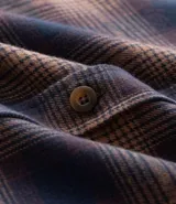 Camisa de manga larga confeccionada en franela de algodón, con diseño de cuadros en tonos marrones y azul marino. Presenta cuello inglés, cierre frontal con botones y dos bolsillos con solapa en el pecho.