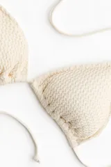 Top de bikini triangular forrado, color beige, con textura gofrada y relleno extraíble. Cuenta con tiras finas para anudar en la nuca y en la espalda.