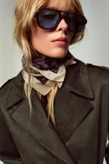 Abrigo largo color marrón oscuro con efecto ante, cuello solapa, manga larga con trabillas en los hombros y bolsillos delanteros de vivo. Presenta un bajo con abertura en la espalda y cierre frontal cruzado con botones, complementado con un cinturón a tono.