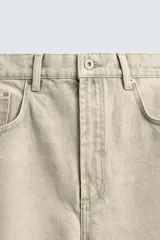 Pantalón jeans de corte recto y tiro medio, confeccionado en denim de algodón color beige con efecto lavado, bolsillos clásicos y cierre frontal con cremallera y botón.