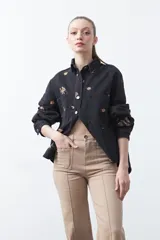 Pantalón de fit recto color beige, confeccionado en cotton spandex. Presenta costuras visibles y bordados decorativos en tono dorado/marrón claro. El ruedo del pantalón tiene un borde festoneado.