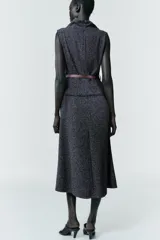 Vestido midi de tejido texturizado en color gris oscuro, con cuello alto fluido, diseño sin mangas y acabados deshilachados. Incluye un cinturón fino de cuero en color marrón con hebilla metálica y cierre de cremallera oculta en la espalda.