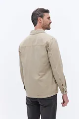 Sobrecamisa de canvas color beige con efecto lavado, de estructura firme y manga larga. Presenta cuello clásico, cierre frontal con botones y un bolsillo frontal en el pecho.