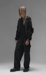 Campera rompevientos negra de calce oversize, confeccionada en microfibra técnica ligera con acabado semi-mate. Presenta capucha integrada, cierre frontal técnico y bolsillos tipo ojal. Destaca por su sistema de frunces elásticos regulables mediante tancas a lo largo de las mangas y el ruedo, permitiendo ajustar el volumen de la prenda.