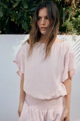Camisa amplia de color rosado, con diseño estilo capa, cuello redondo y manga corta amplia. Cuenta con un bajo ajustable mediante lazada lateral.