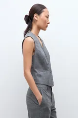 Chaleco sastrero de corte entallado con escote en V, cierre frontal con botones y bolsillos laterales simulados. Presenta un estampado de microcuadros en tonos grises.