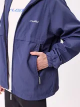 Campera rompevientos Rusty de color azul, con capucha ajustable, cierre frontal completo y bolsillos laterales. Presenta puños elásticos y logo de la marca estampado en el pecho.