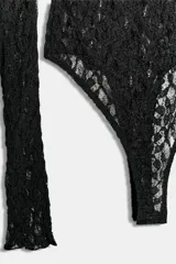 Body de encaje negro con mangas largas, cuello redondo y espalda descubierta. Cuenta con cierre en el bajo.