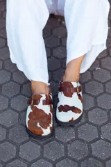 Suecos con capellada de cuero con estampado de vaca, plantilla anatómica y hebilla lateral ajustable.