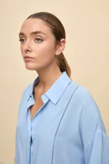 Camisa de calce relajado color celeste, con mangas 3/4, cuello clásico y cierre frontal con botones. Presenta detalles calados en el frente y en las mangas que aportan un acabado delicado al diseño.