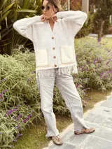 Cardigan de punto color beige con escote en V, cierre frontal con botones, bolsillos delanteros aplicados y detalle de flecos en el ruedo.