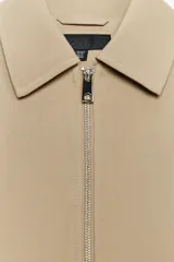 Chaqueta bomber negra con cuello solapa, manga larga abullonada y puños elásticos. Presenta falsos bolsillos de doble vivo en la parte delantera y cierre frontal con cremallera.