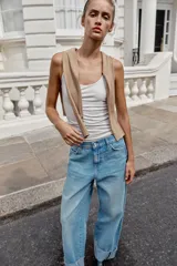 Jeans baggy de tiro medio con pernera holgada, diseño de cinco bolsillos y bajo acabado en vuelta. Cuenta con cintura elástica en la espalda y cierre frontal con cremallera y botón.