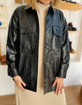 Sobrecamisa negra de ecocuero con cuello clásico, cierre frontal con botones, mangas largas y bolsillos de parche en el pecho.