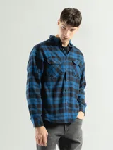 Camisa de franela a cuadros color celeste, gris y negro, de manga larga con dos bolsillos frontales con solapa abotonada.