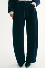 Jean de denim rígido azul oscuro, con corte holgado y diseño curvo en las piernas. Presenta cintura estándar con cordón ajustable, cierre con botón y bolsillos clásicos.