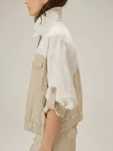 Chaquetas de lino bicolor en tonos blanco y beige, con diseño holgado, cuello alto, cierre frontal de botones, bolsillos con solapa en el pecho y mangas cortas con presilla y botón.