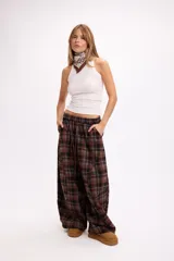 Pantalon de corte oversize y tiro medio, confeccionado en tela con estampado de cuadros en tonos marrones y negros. Presenta una silueta amplia y holgada con cintura elástica y cordón ajustable.