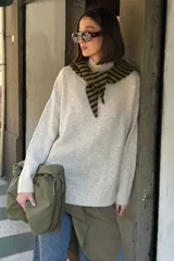 Sweater de punto color beige melange, de corte holgado, con cuello alto, mangas largas y costura central visible en el frente.