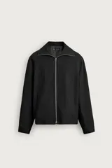 Sobrecamisa relaxed fit de Zara confeccionada en tejido negro con estructura diagonal. Presenta cuello subido, manga larga, bolsillos de vivo en la cadera y cierre frontal con cremallera.