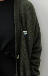 Cárdigan verde oliva de lana con botones dorados, bolsillos delanteros y corte holgado.