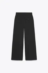 Pantalón de vestir marrón oscuro, tiro alto, con pernera ancha y pinzas frontales. Presenta un bolsillo con tapeta en la parte superior delantera.