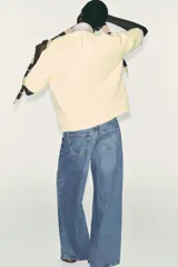 Jersey de punto color amarillo pálido, con cuello redondo y mangas cortas. Presenta un calce oversize y aberturas caladas en los laterales inferiores.