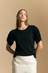 Remera de algodón color negro, con cuello redondo y mangas cortas abullonadas con frunces en los hombros.