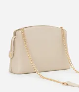 Cartera bandolera pequeña de diseño estructurado en color beige, confeccionada en poliuretano con acabado liso. Presenta un diseño geométrico con costuras en relieve en la parte frontal, cierre superior con cremallera y una elegante correa de cadena metálica en tono dorado.