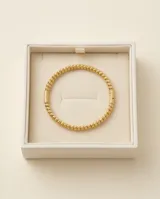 Pulsera esclava de acero con baño de oro, compuesta por pequeñas esferas texturizadas y un detalle central cilíndrico estriado.