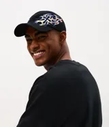 Gorra de algodón negra con visera curva y diseño estructurado, que presenta un bordado lateral con detalles tribales de fuego en tonos azules y dorados.