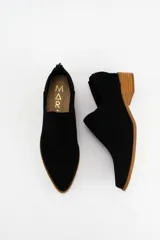 Zapato tipo botineta de gamuza negra con diseño de corte lateral, taco bajo de madera y cierre en la parte trasera.