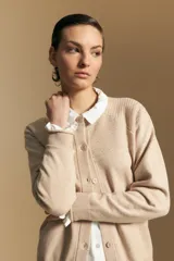 Cardigan de tejido de punto color beige, con cierre frontal de botones, cuello redondo y terminaciones acanaladas en puños y ruedo. Presenta un diseño con textura en la parte superior del pecho.