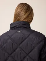 Campera larga acolchada con diseño de rombos, cierre frontal completo y cuello alto. Presenta puños elásticos y un pequeño logo aplicado en el pecho.