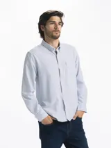 Camisa celeste y blanca a rayas verticales, de manga larga y corte clásico. Tiene cuello abotonado y bolsillo en el pecho.